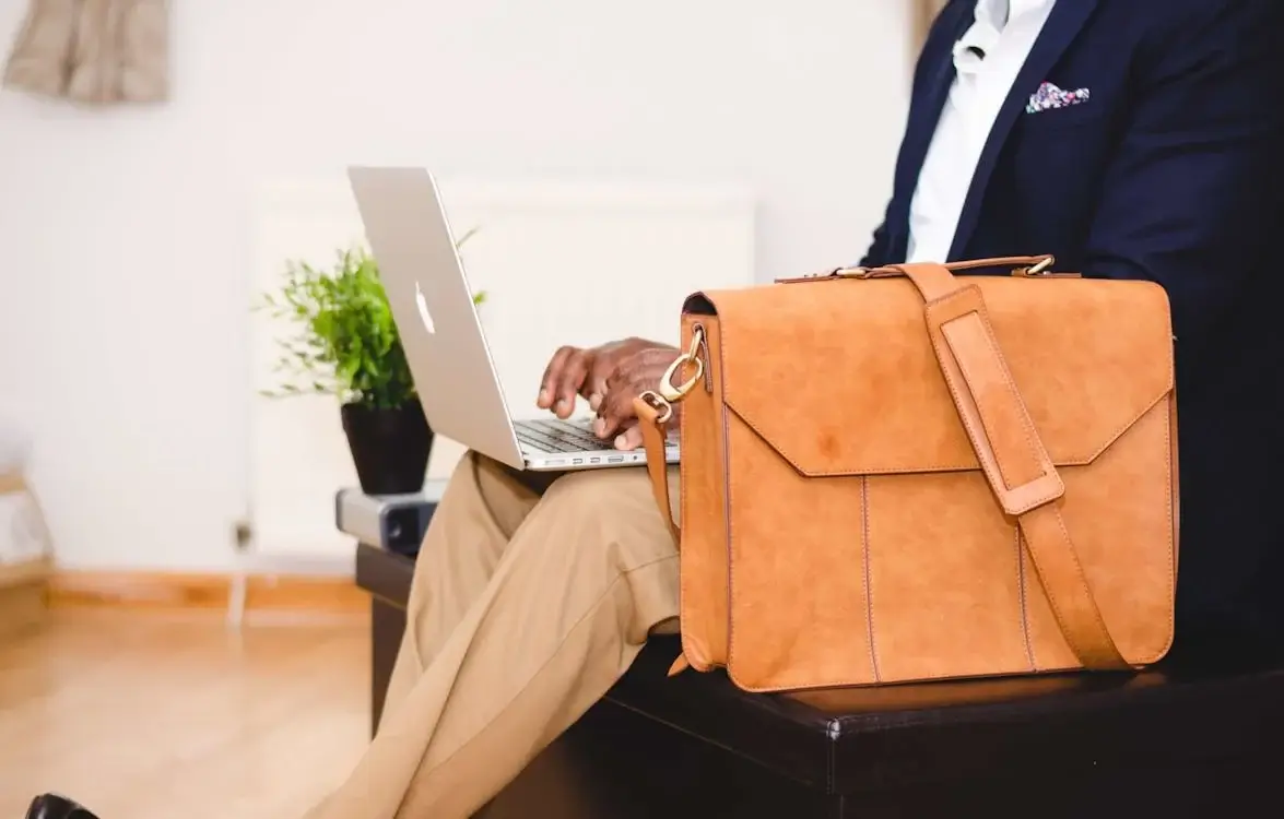 person wearing blue jacket, seated next to tan briefcase, working on laptop person wearing blue jacket, seated next to tan briefcase, working on laptop