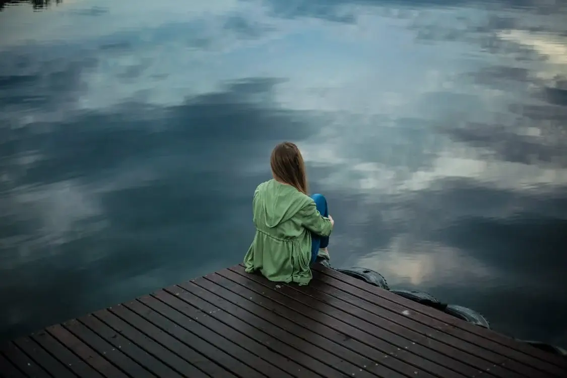 depression concept image - woman sitting alone on edge of dock