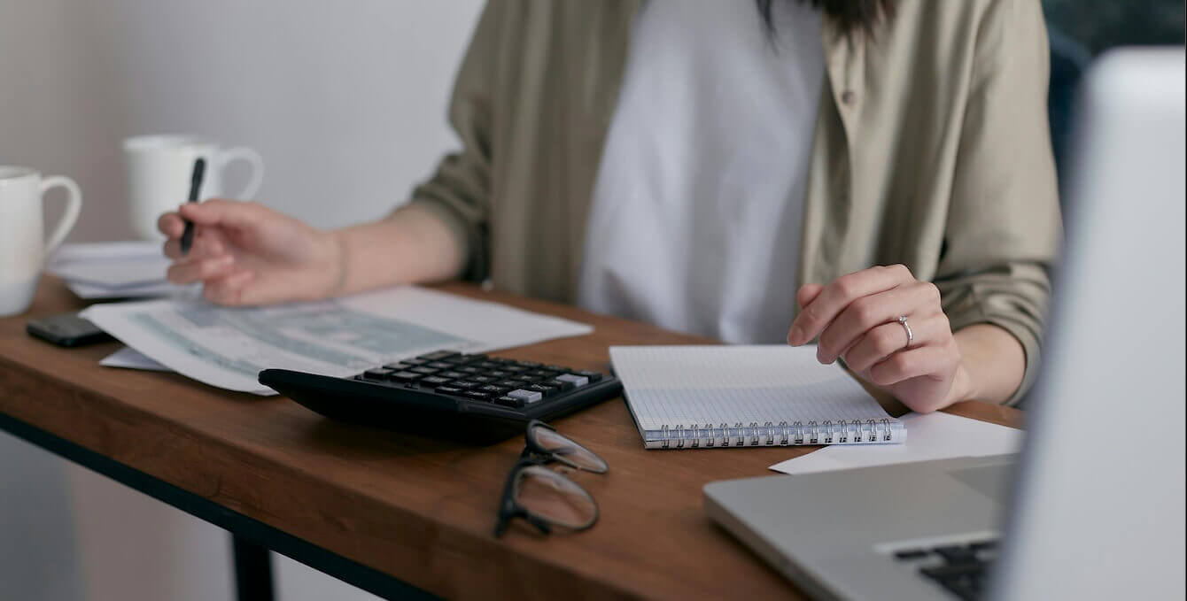 A desk with a laptop and glasses on it, and a person going over some paperwork